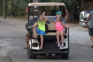 two kids riding on the back of a golf cart